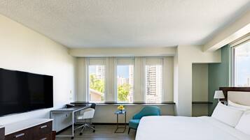 A hotel room with a bed, a desk, a chair, a TV, and a window with a view of buildings.