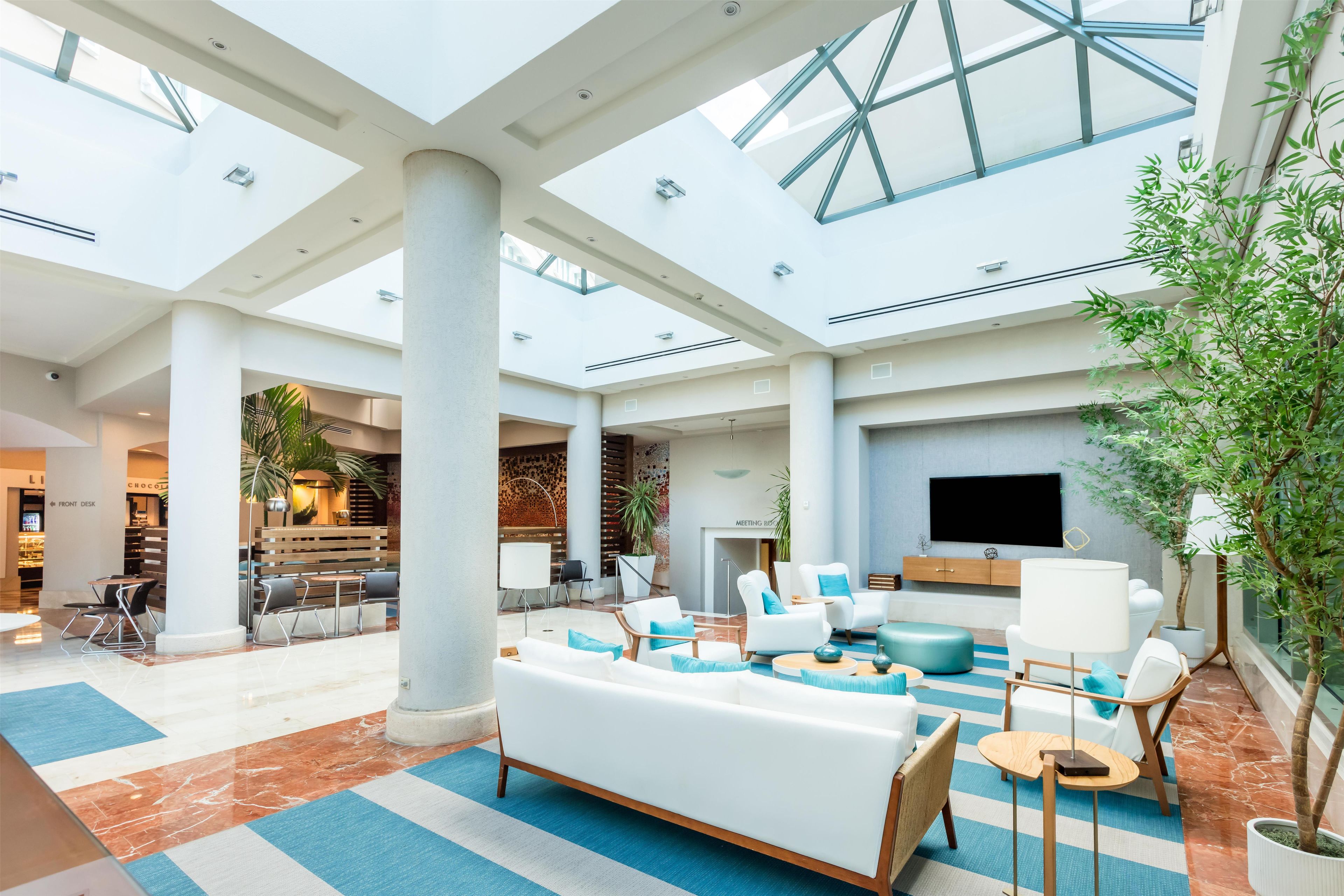 Un vestíbulo espacioso con techo alto, ventanas grandes y una zona de estar con sofás y sillones.