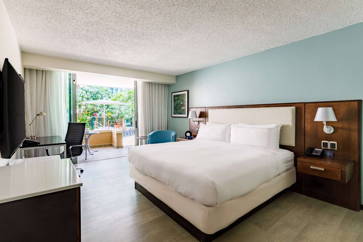 A hotel room with a large bed, a desk, a chair, a TV, and a window with curtains.