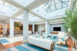 Een ruime lobby met een hoge plafond, grote ramen en een zithoek met banken en stoelen.