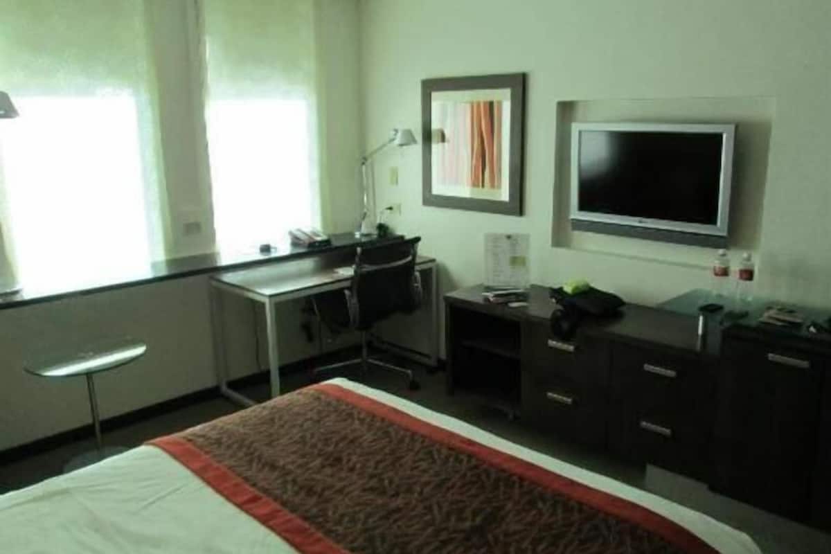 A hotel room with a bed, desk, chair, TV, and a window.