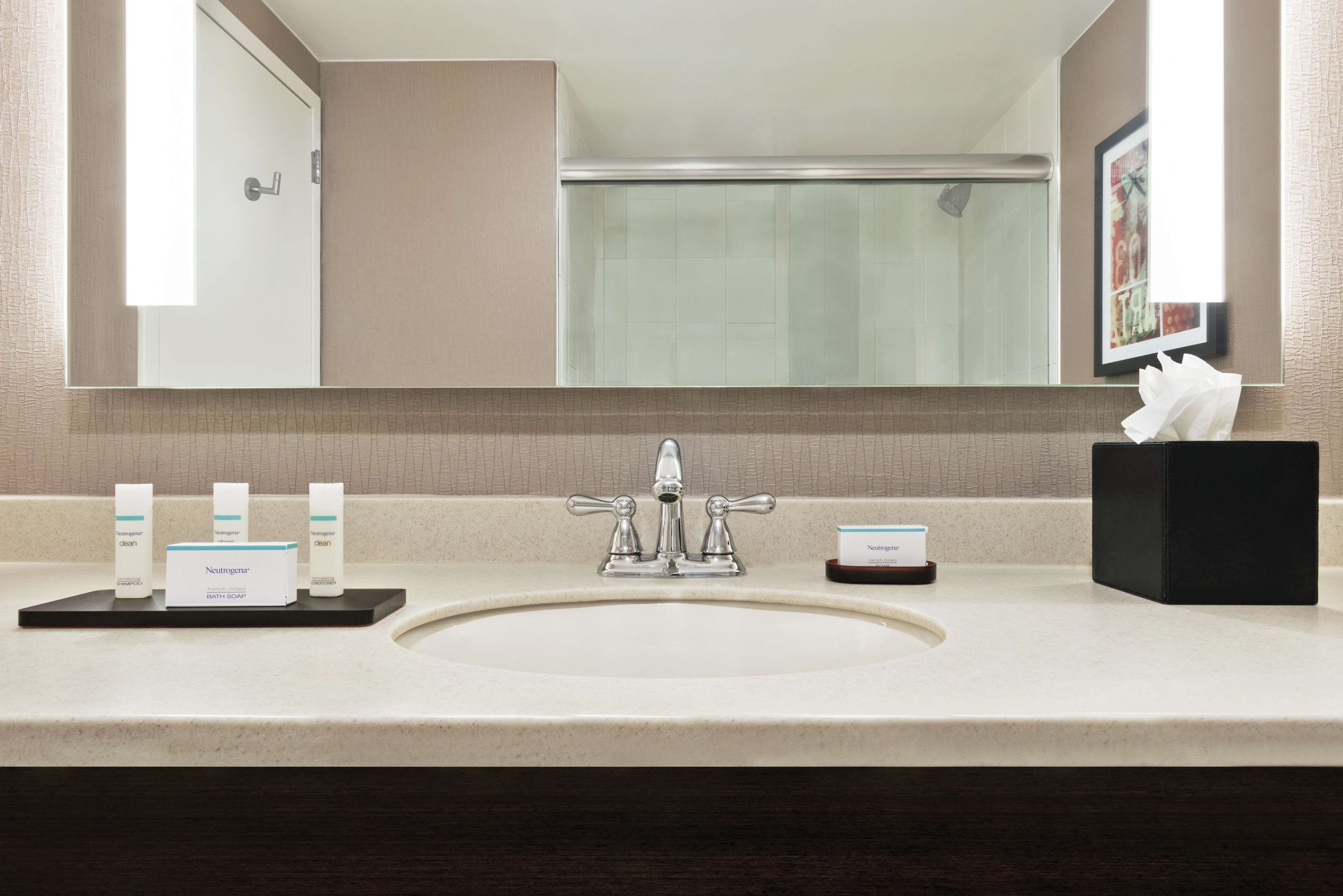Une salle de bain avec un grand miroir, un lavabo et trois bouteilles de savon liquide pour le bain de la marque Neutrogena.