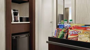 Habitación de hotel con minibar, cafetera y snacks como papas fritas y refrescos.