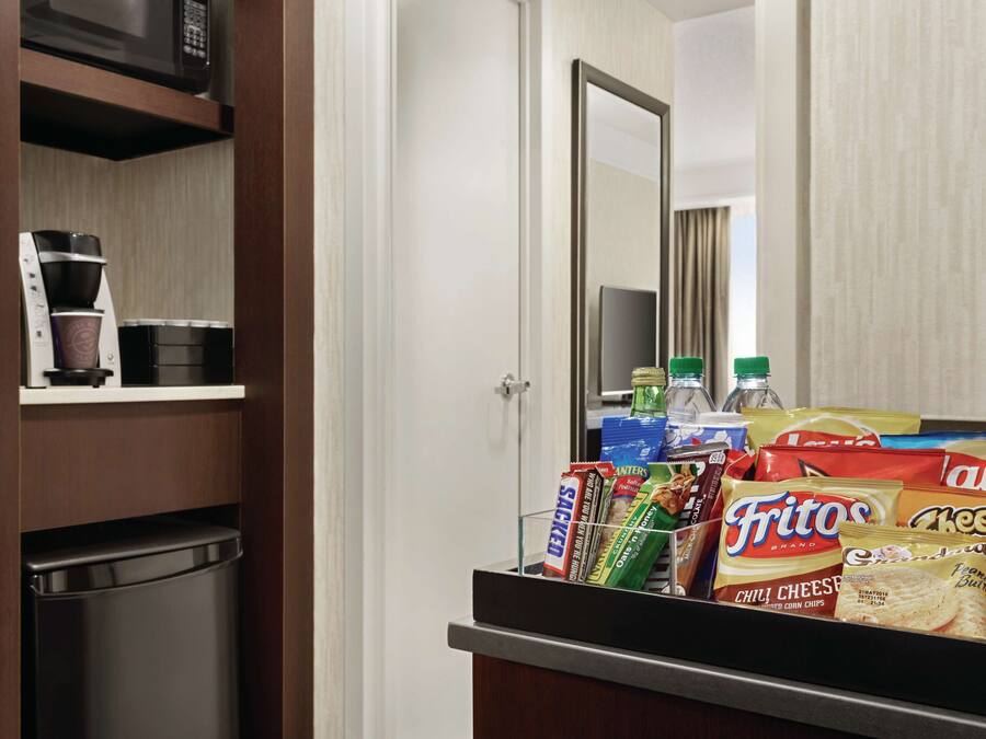 Habitación de hotel con minibar, cafetera y snacks como papas fritas y refrescos.
