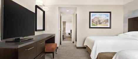 A hotel room with a flat-screen TV, a desk with drawers, a bench, two beds, and a framed picture on the wall.
