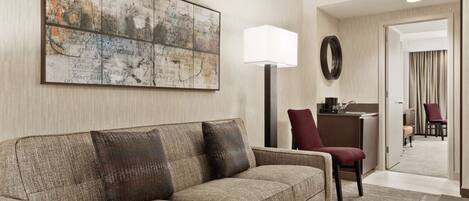 A hotel room with a large wall map, a sofa, a desk with a chair, and a mirror.
