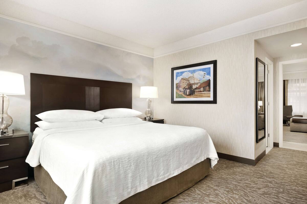 Une chambre d’hôtel avec un grand lit, une table de chevet, une lampe et un tableau encadré au mur.