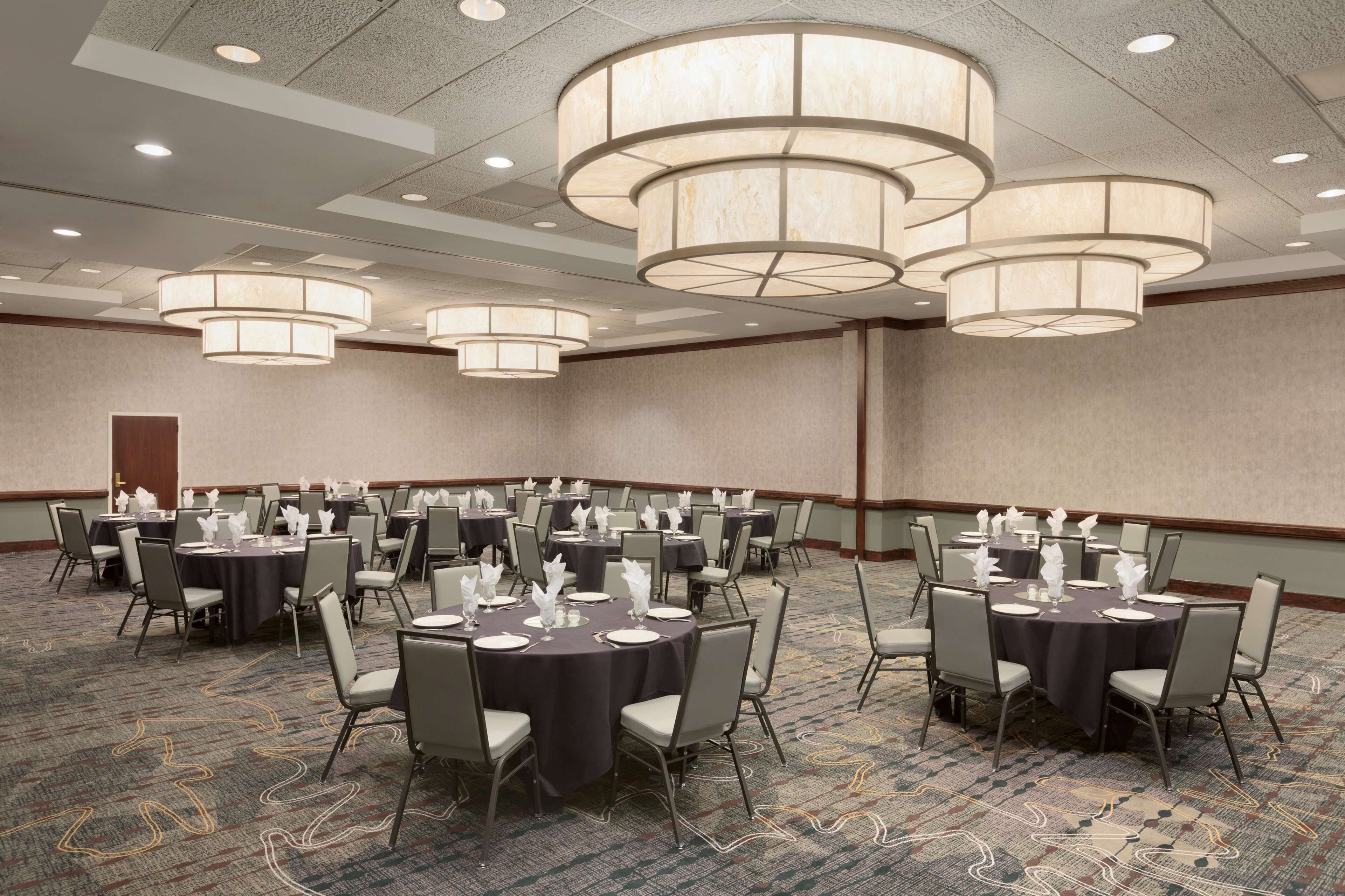 A conference room with multiple tables set for a meeting, equipped with chairs and tables, and large ceiling lights.