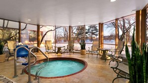 Zona de piscina interior climatizada con jacuzzi, asientos y ventanas amplias.
