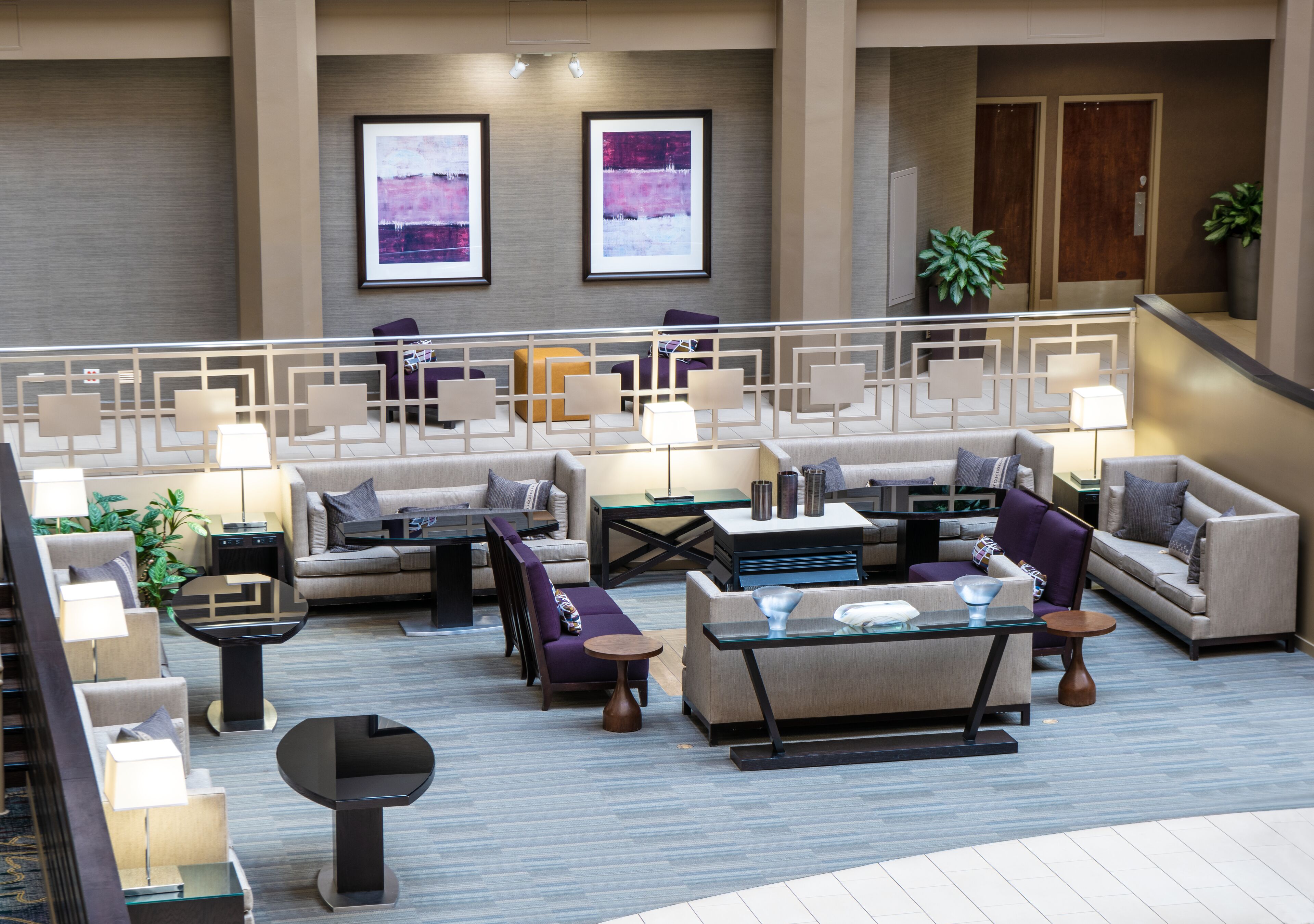 Een ruime lobby met meerdere zithoeken, inclusief banken en fauteuils, gearrangeerd rond een centrale salontafel. Twee ingelijste kunstwerken hangen aan de muur, en er is een trap in de achtergrond zichtbaar.