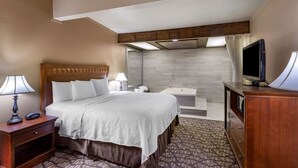 A hotel room with a bed, bedside lamps, a television, a desk, and a bathroom with a bathtub. - Best Western Dunmar Inn (Evanston)