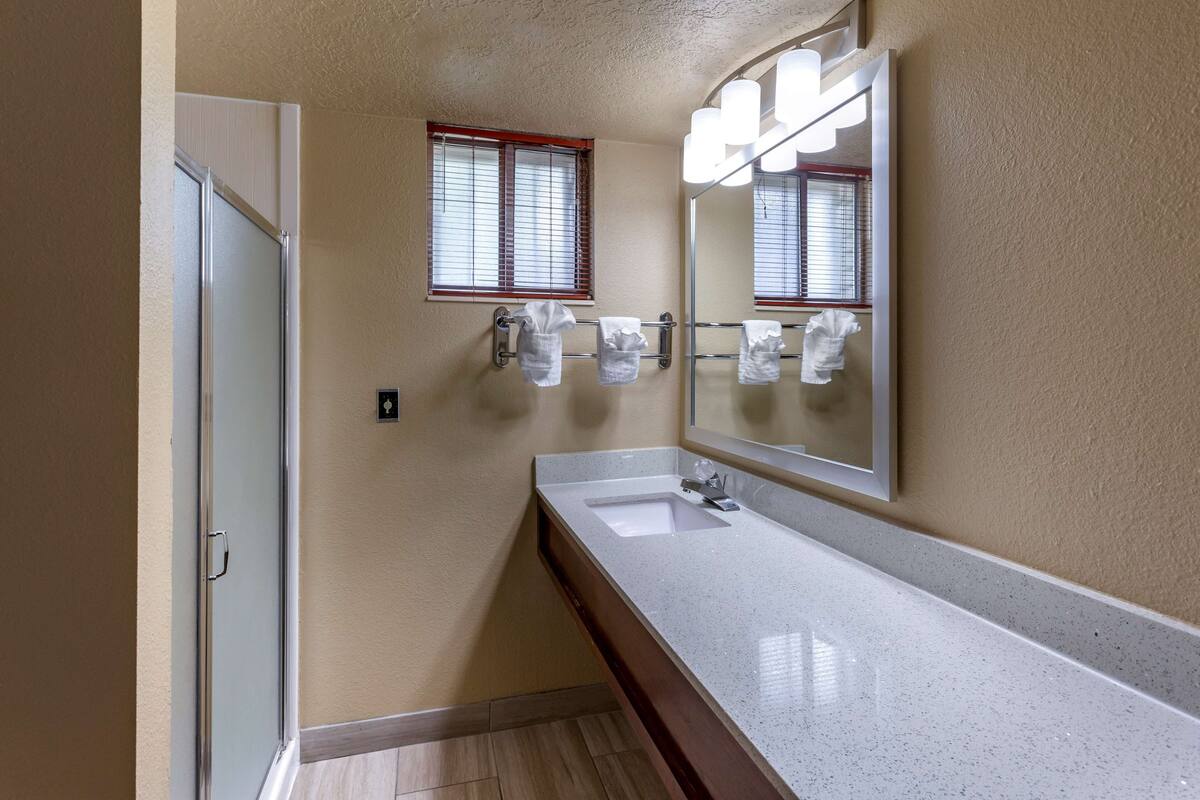 Ein Badezimmer mit einem weißen Waschbecken, einem Spiegel und einem Fenster mit Jalousien.