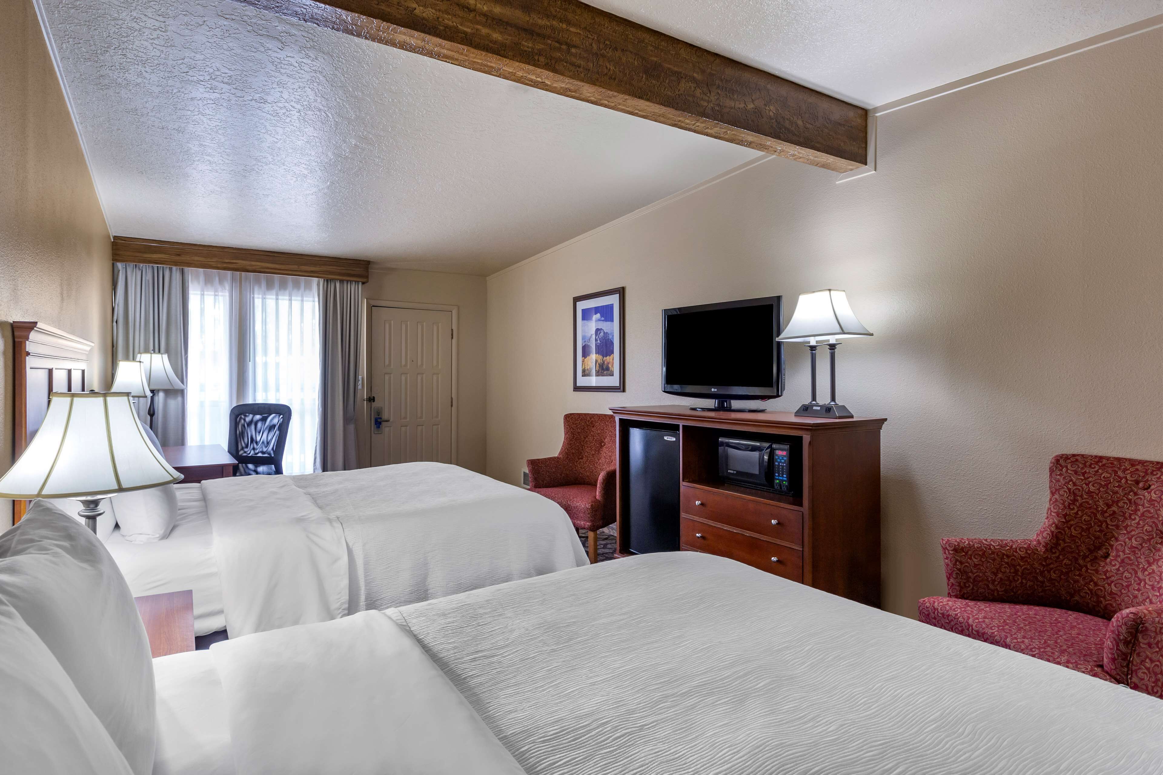 Habitación de hotel con dos camas, un escritorio, televisor y cómoda.