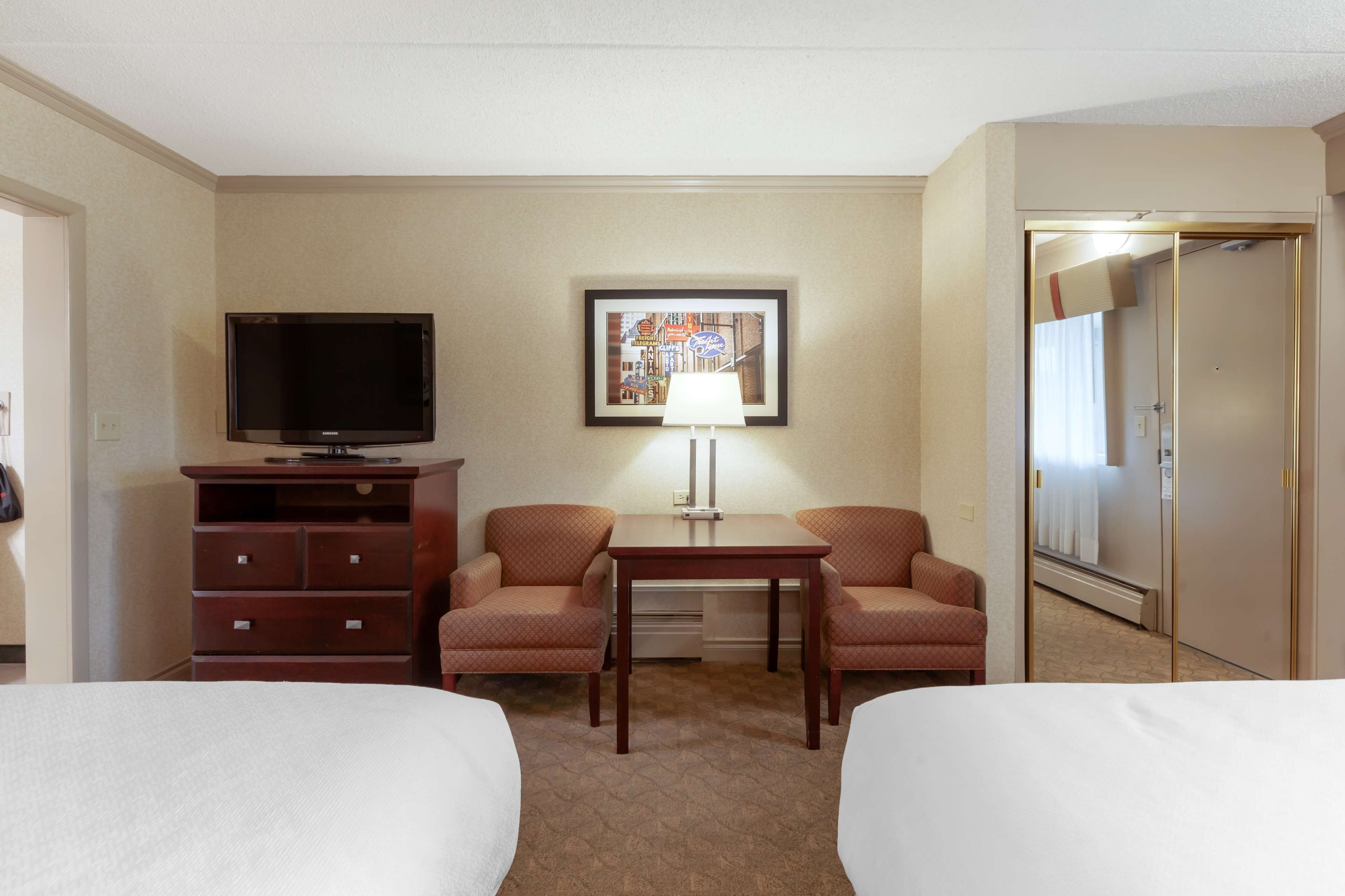 A hotel room with two beds, a TV, a desk with a lamp, a dresser, and a framed picture on the wall.