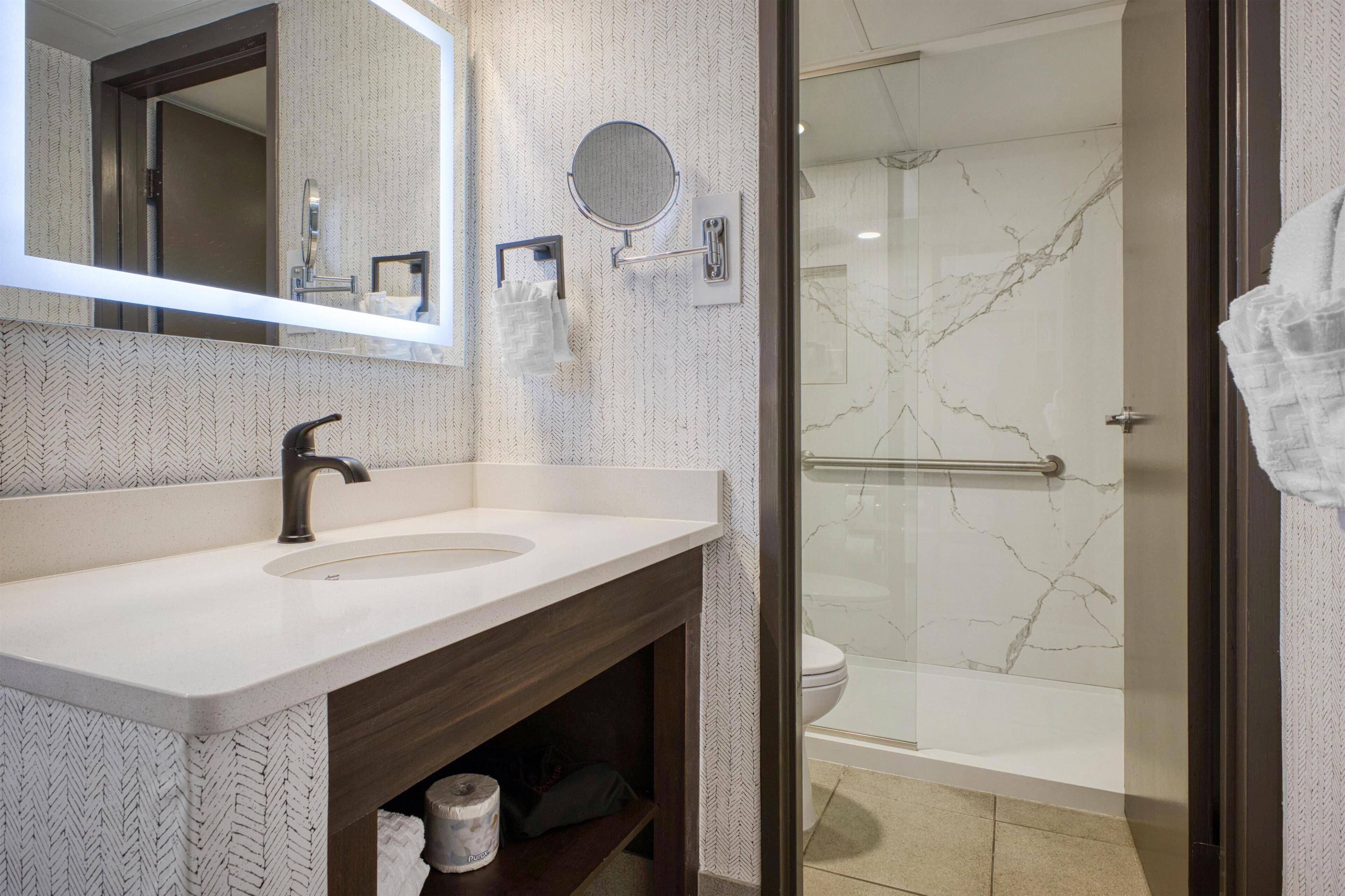 Une salle de bain comprenant un lavabo, un miroir, un porte-serviettes, des toilettes et un espace douche.