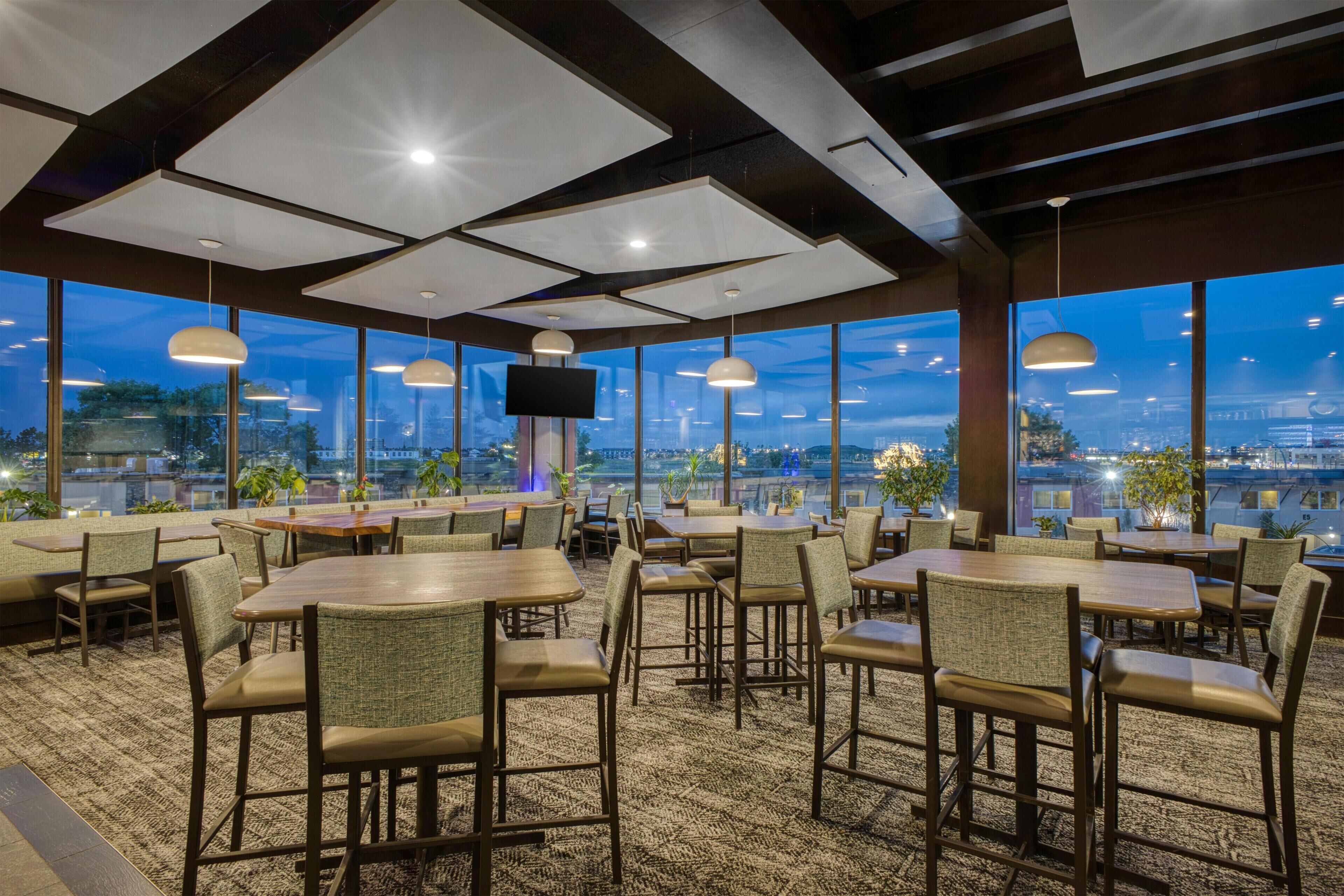 Un restaurante con vistas a la ciudad al anochecer, con mesas y sillas dispuestas para comer.