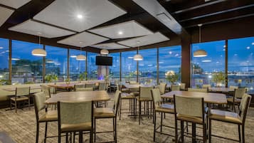 Un restaurante con vistas a la ciudad al anochecer, con mesas y sillas dispuestas para comer.