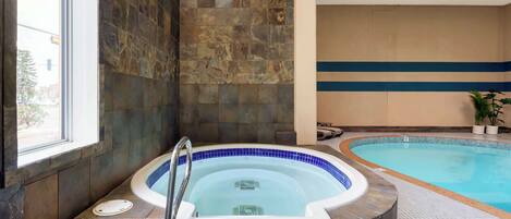 A spa area with a hot tub and a swimming pool, stone walls, and a ceiling fan.