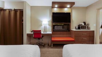 A hotel room with two beds, a desk with a chair, a television, a microwave, and a small kitchenette.