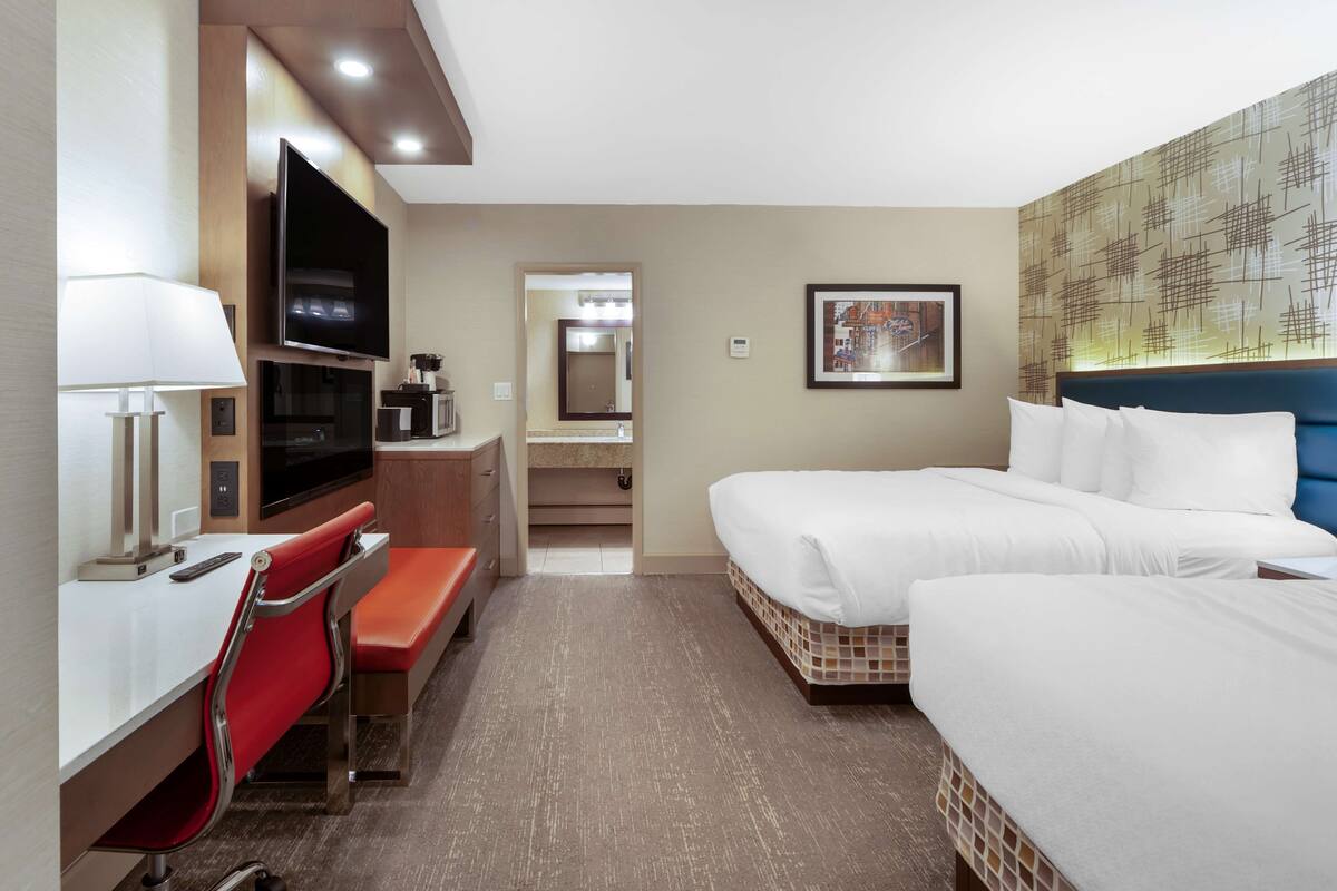 Habitación de hotel con cama, televisor, escritorio con silla y baño visible a través de una puerta abierta.