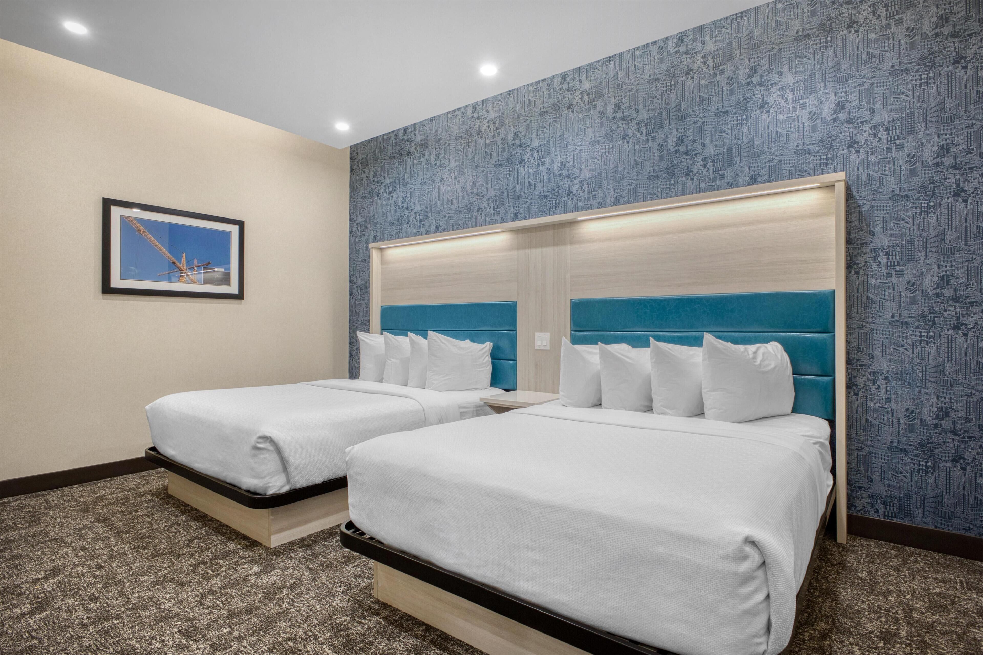 A hotel room with two beds, a cityscape wallpaper, and a framed picture on the wall.