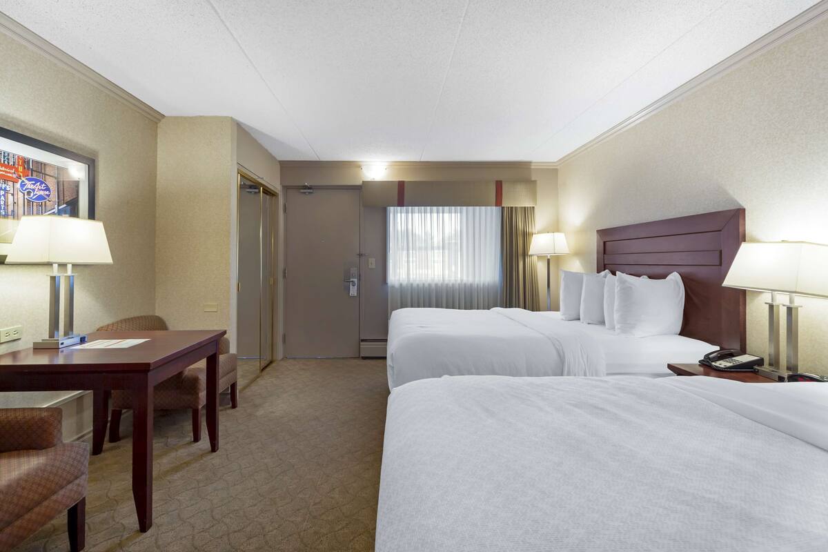 Habitación de hotel con dos camas, un escritorio, una silla, un teléfono y una ventana con cortinas.
