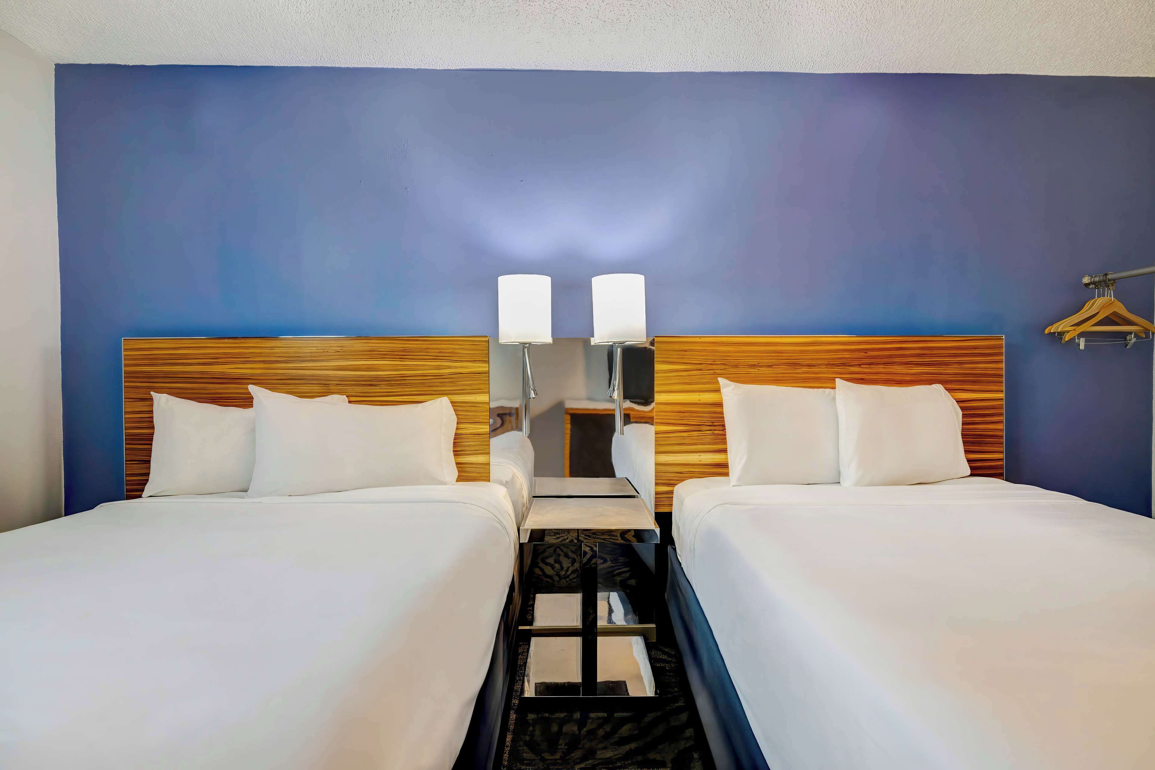 Een hotelkamer met twee bedden, een houten hoofdeinde, een kleine tafel en een wandlamp.