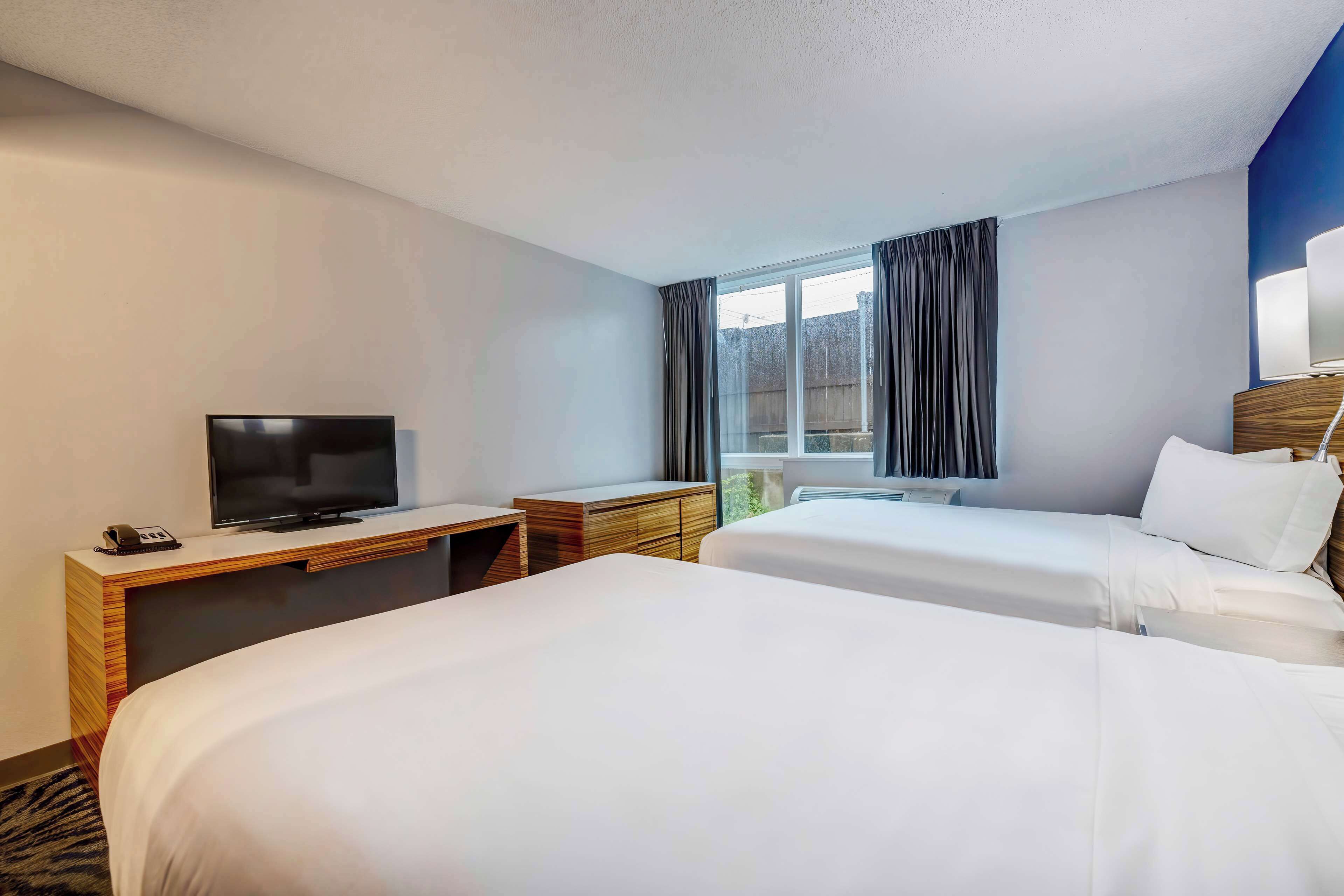 Une chambre d’hôtel avec deux lits, une télévision, un bureau et une fenêtre avec des rideaux.