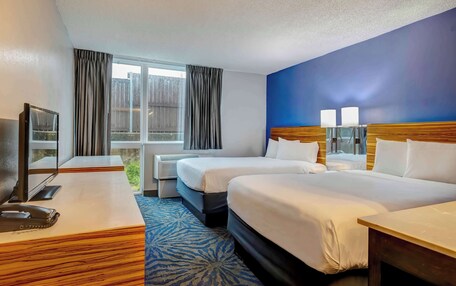 A hotel room with two beds, a desk, a television, and a window with curtains.