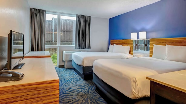A hotel room with two beds, a desk, a television, and a window with curtains.