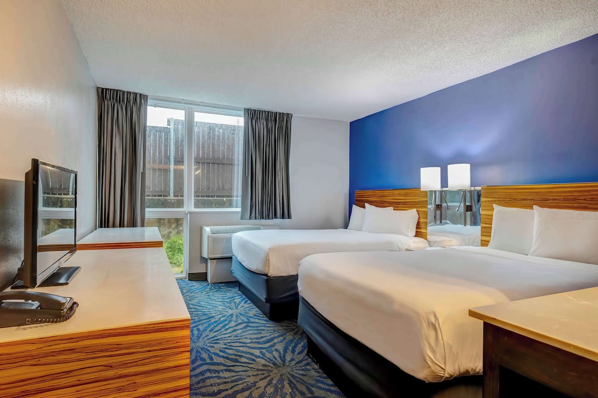 A hotel room with two beds, a desk, a television, and a window with curtains.