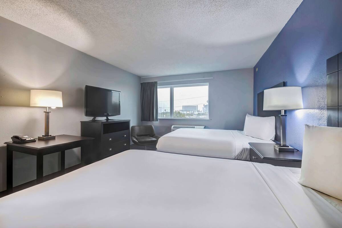 A hotel room with two beds, a desk with a lamp, a chair, a TV, and a window with curtains.