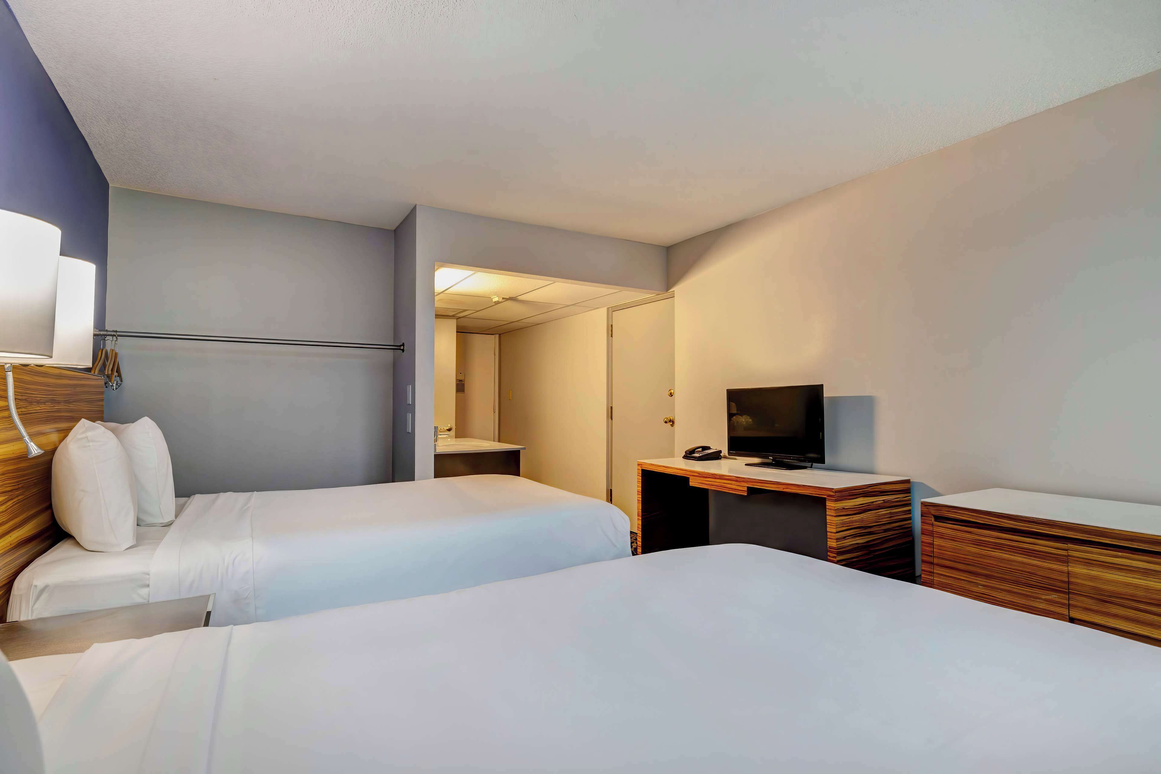 A hotel room with two beds, a desk, a television, and a mirror.