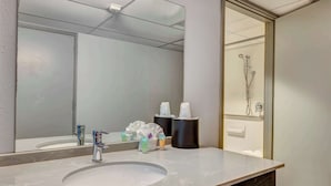 A hotel bathroom with a large mirror, a sink, and a shower area.