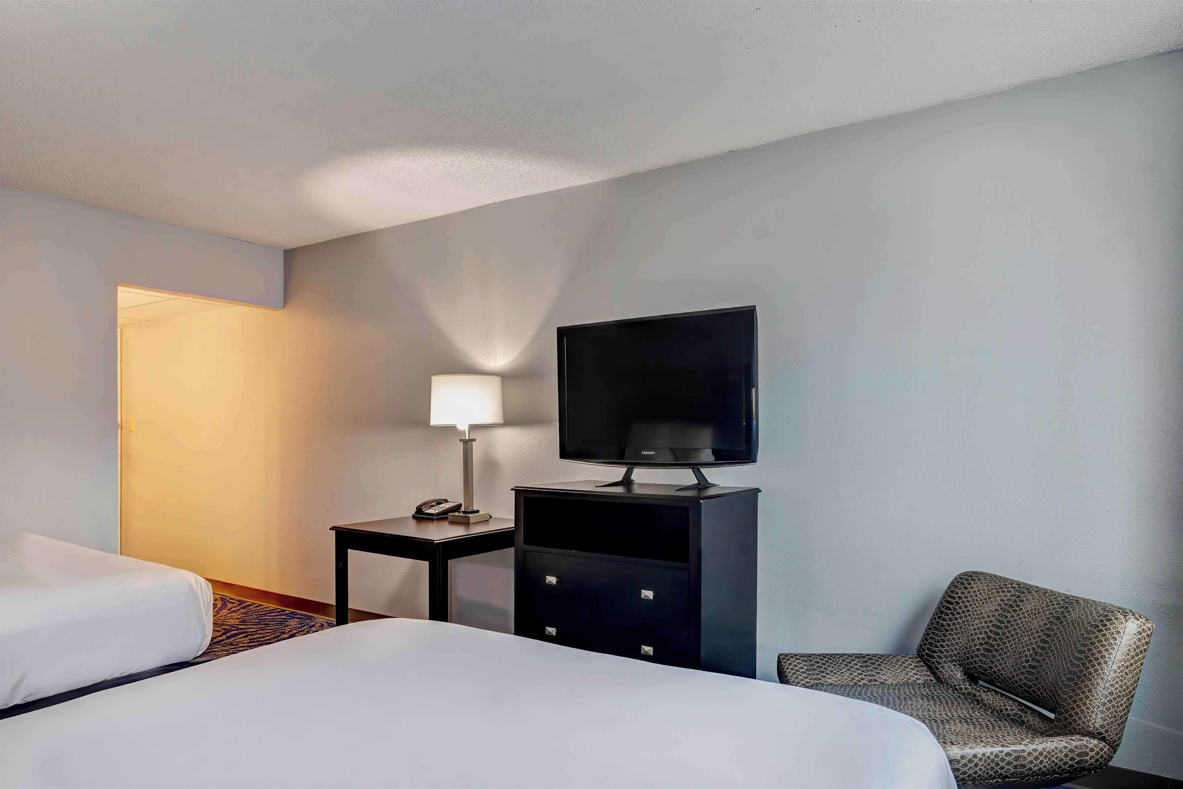 Una habitación de hotel con una cama, un televisor en un mueble bajo, una silla y un escritorio con una lámpara.