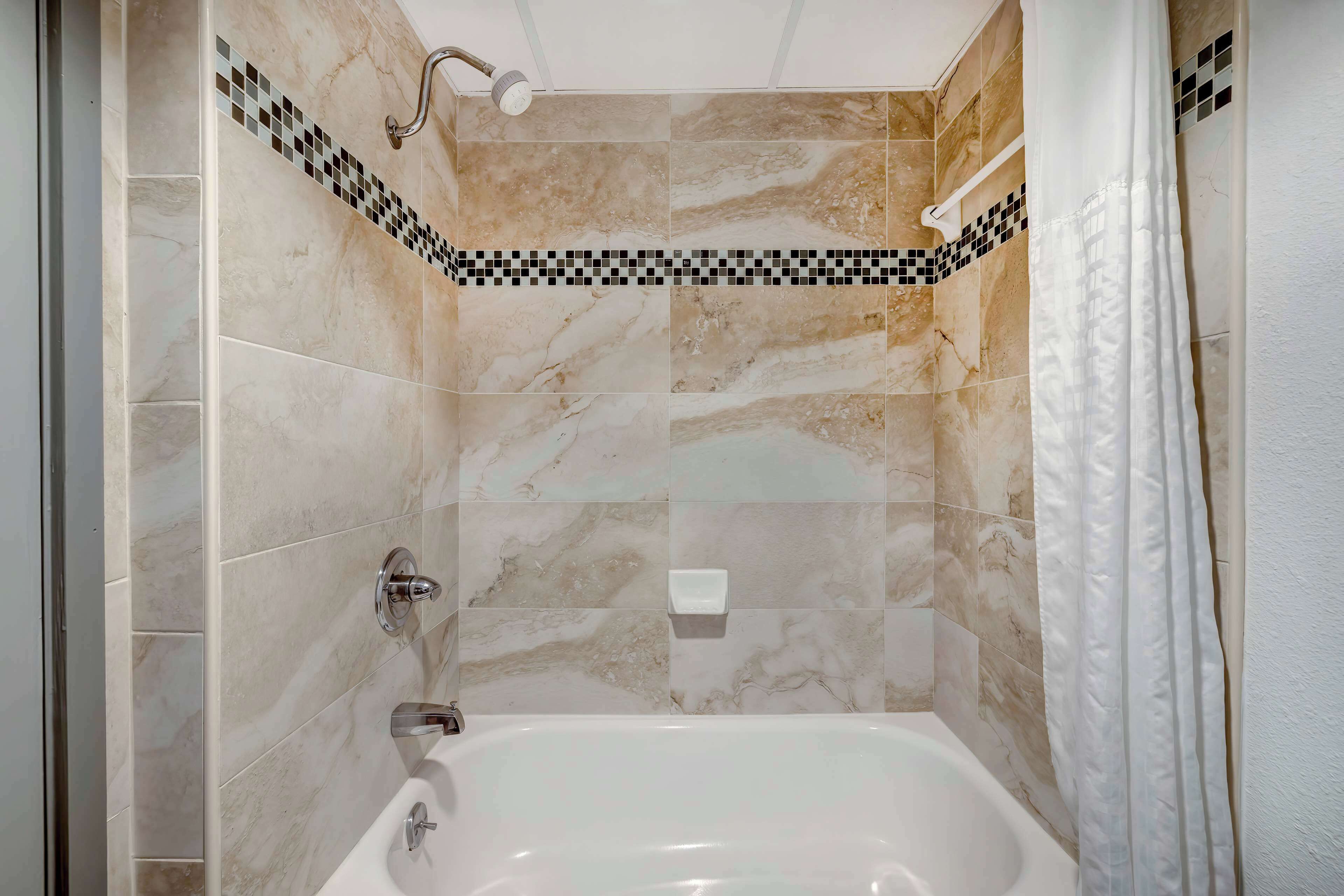 Un baño con bañera, paredes de azulejos y zona de ducha.