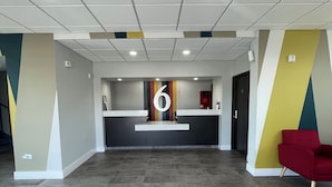A spacious lobby with a reception desk, a red chair, and a large number '6' on the wall.