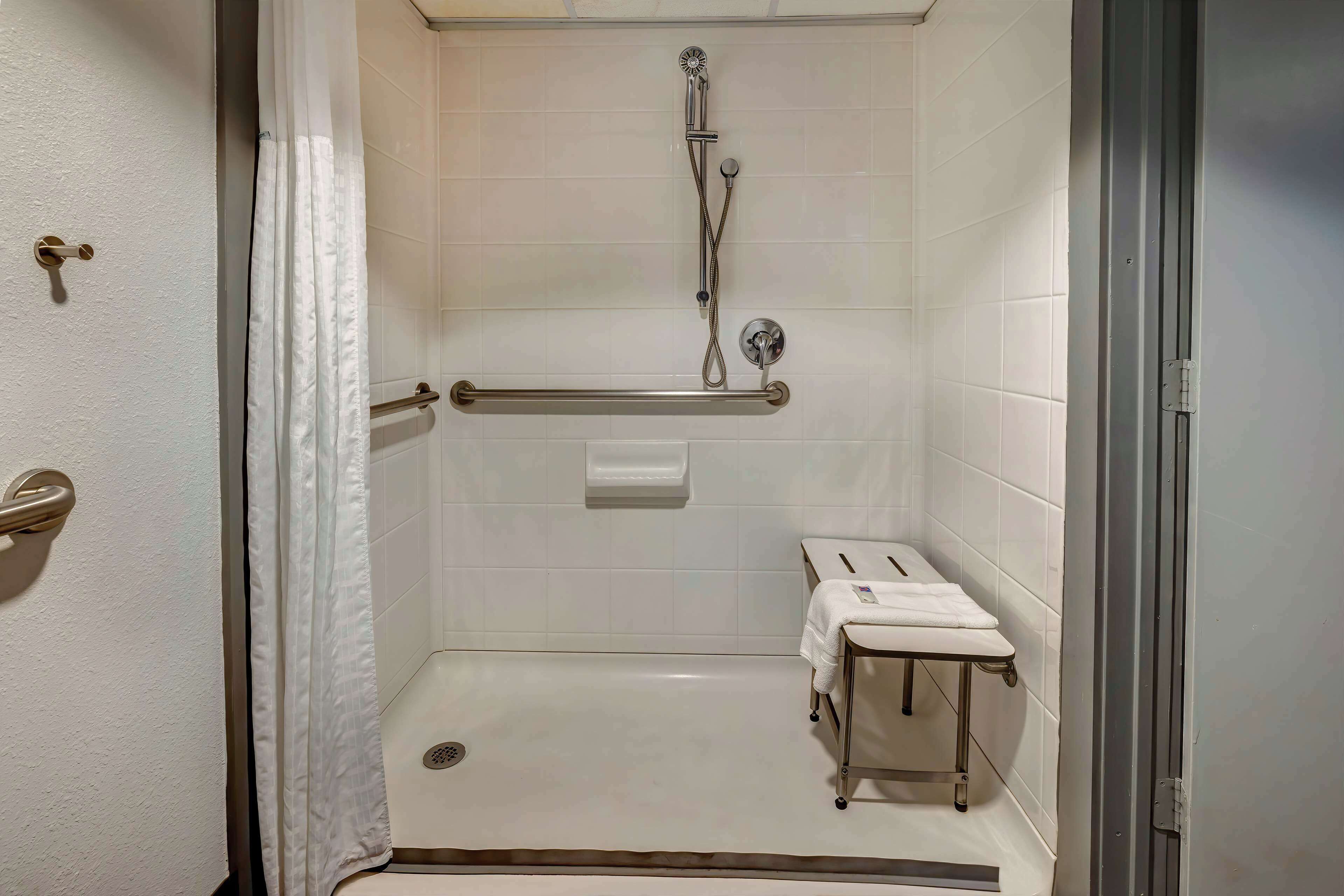 A walk-in shower with a grab bar, a towel rack, and a small table.