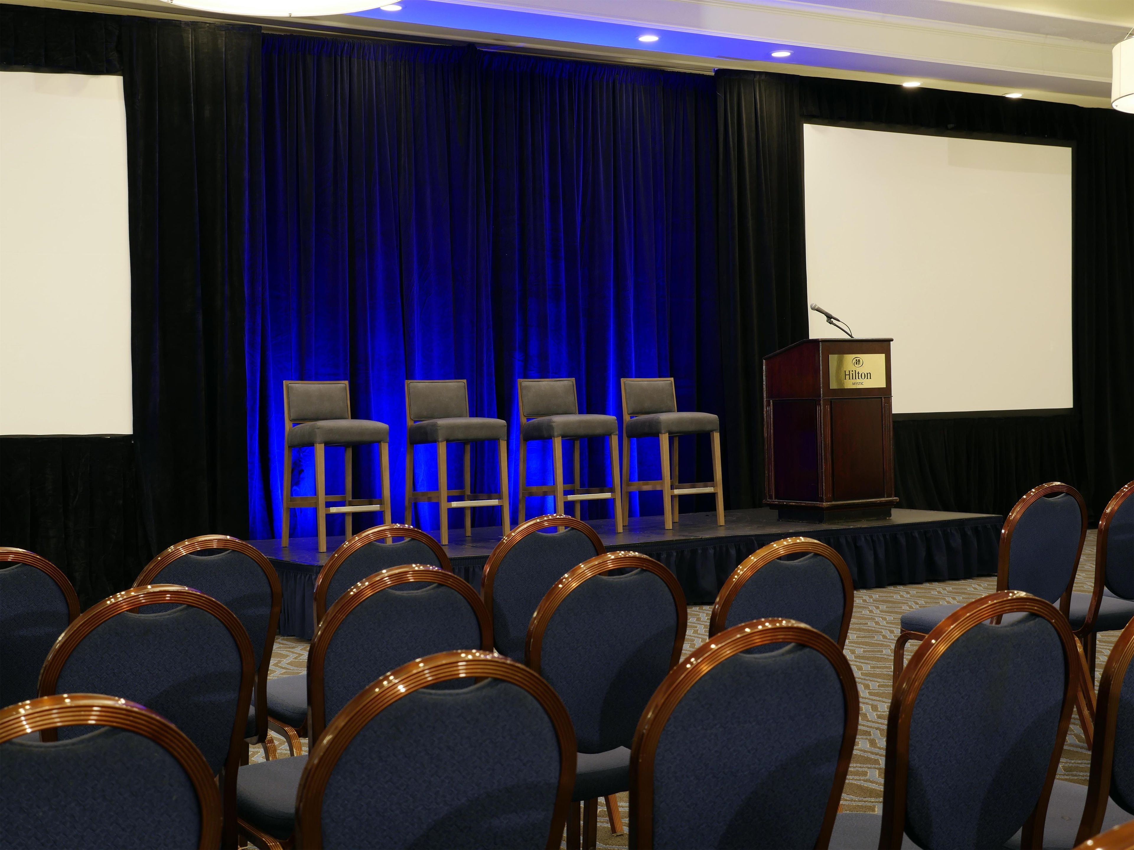 A conference room with a stage, a podium, and rows of chairs.