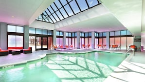 An indoor swimming pool with clear glass ceilings, sunlit areas with lounge chairs, and a visible lifeguard station. - Hilton Mystic (Mystic)