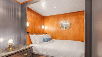 Un dormitorio con cabecera de madera, un espejo redondo, una cama con ropa blanca y una mesita de noche con lámpara.