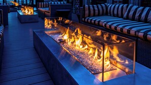 A modern outdoor seating area with a glass fire feature and a striped sofa. - Hilton Mystic (Mystic)
