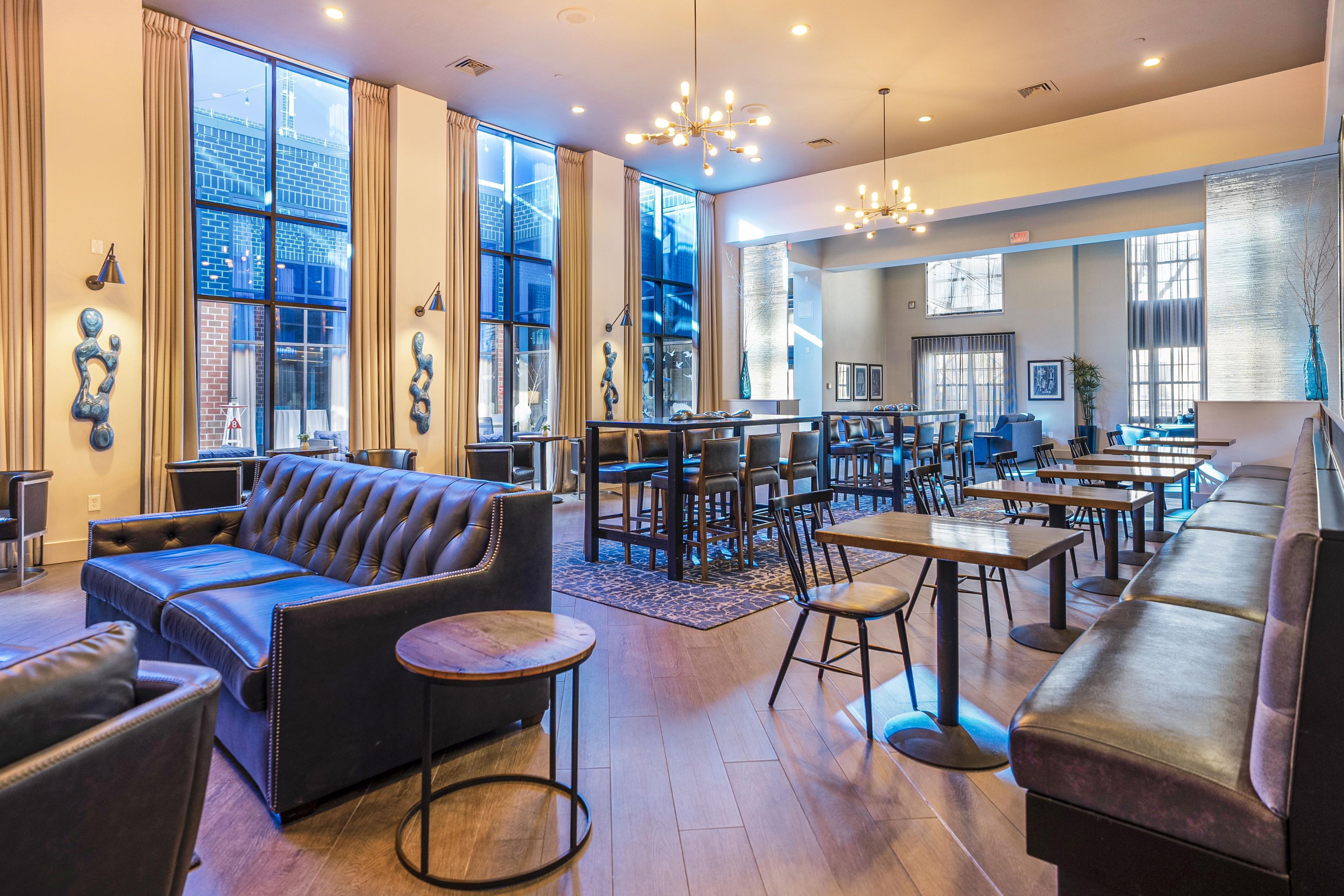 A spacious lounge area with leather sofas, round tables, and a large window offering a view of the cityscape.