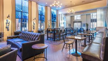 A spacious lounge area with leather sofas, round tables, and a large window offering a view of the cityscape.