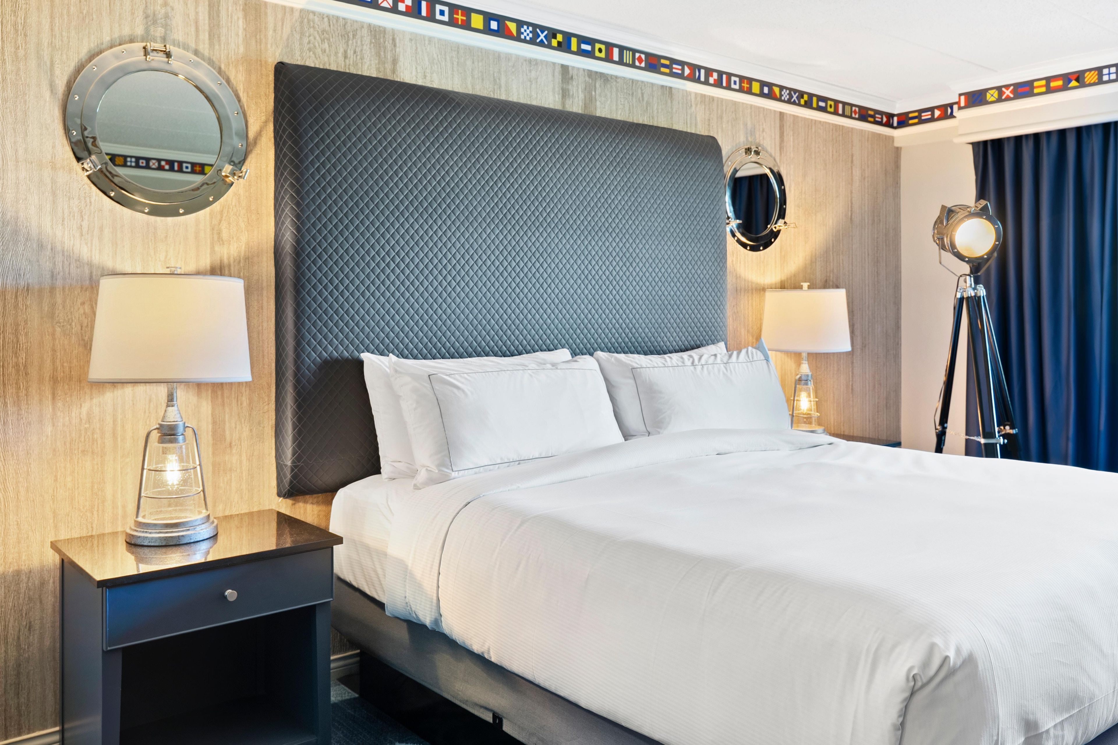Habitación de hotel con una cama grande, dos mesitas de noche, un espejo redondo y una lámpara en cada mesita.