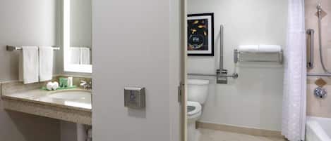 A bathroom with a sink, toilet, shower, and a handrail.