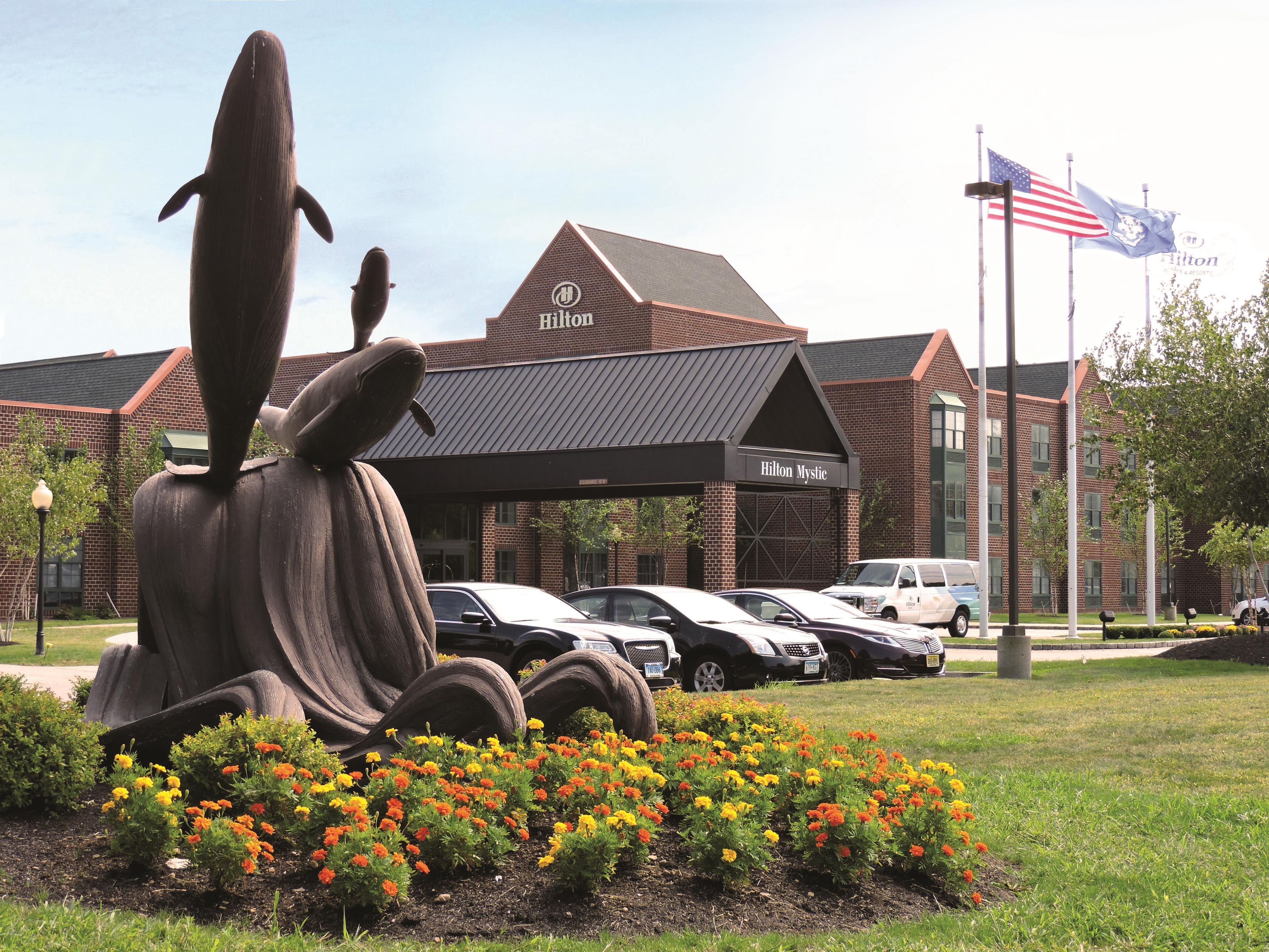 A Hilton Mystic hotel with a large whale sculpture in the foreground, surrounded by colorful flowers.