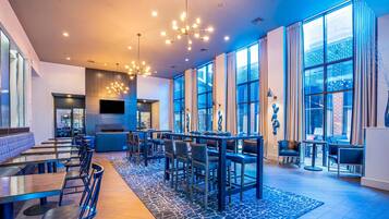 A modern hotel lobby with a long reception desk, seating area, and large windows offering views of the city.