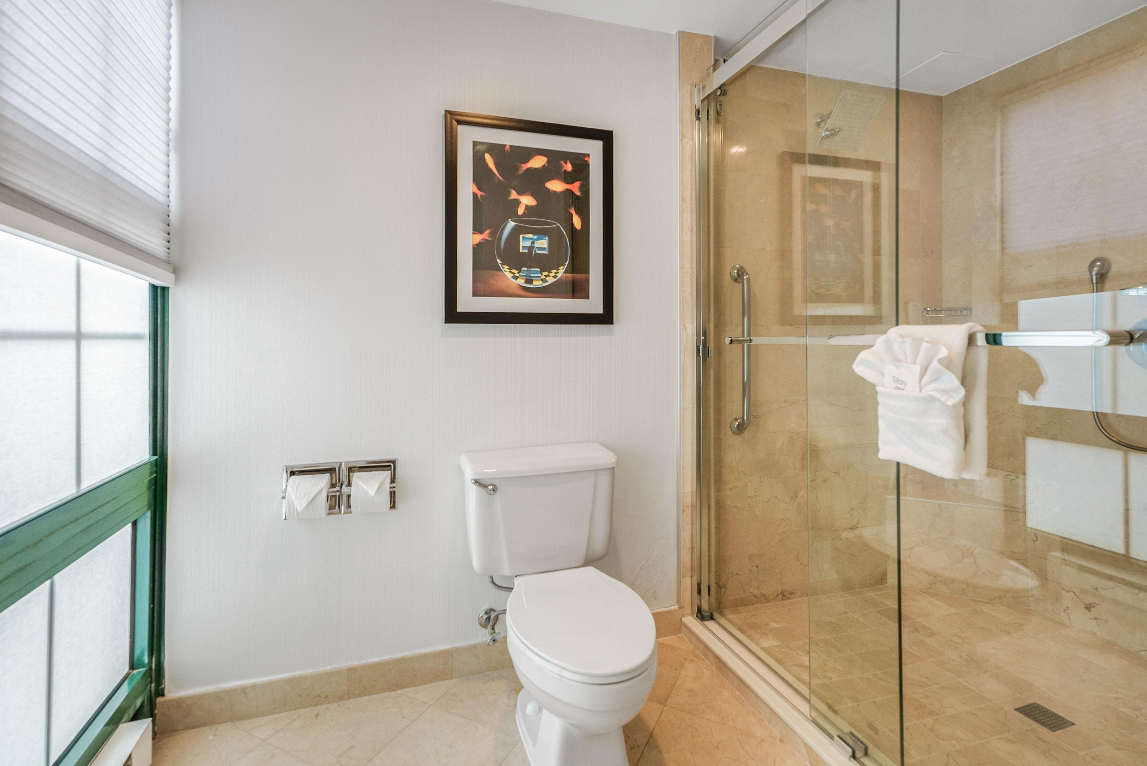 A modern bathroom with a toilet, a glass shower enclosure, and a framed artwork on the wall.
