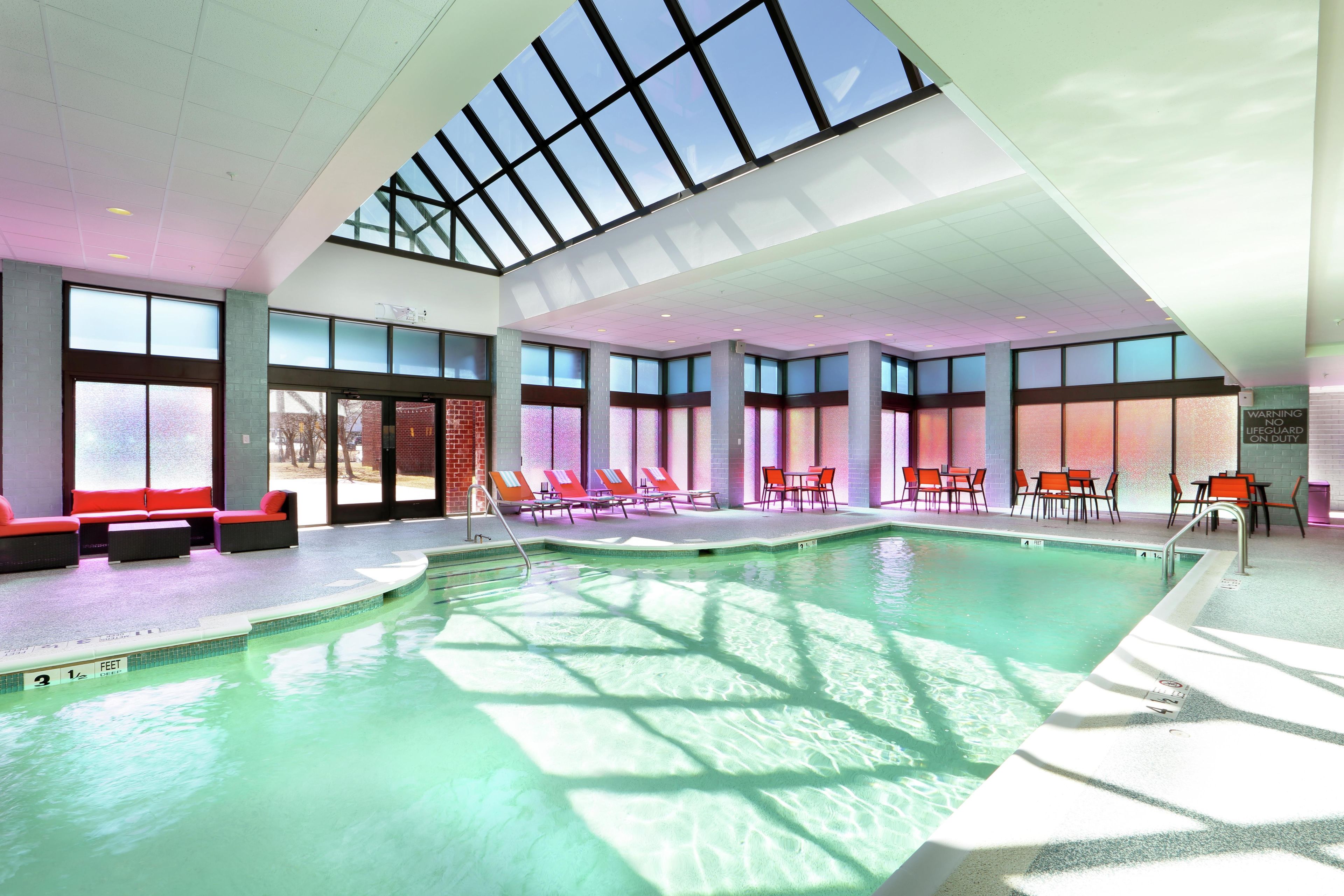 An indoor swimming pool with clear glass ceilings, sunlit areas with lounge chairs, and a visible lifeguard station.